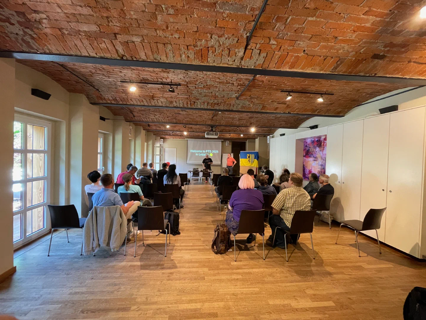The opening session of PTS 2025, attendees seated in a brick-ceilinged room