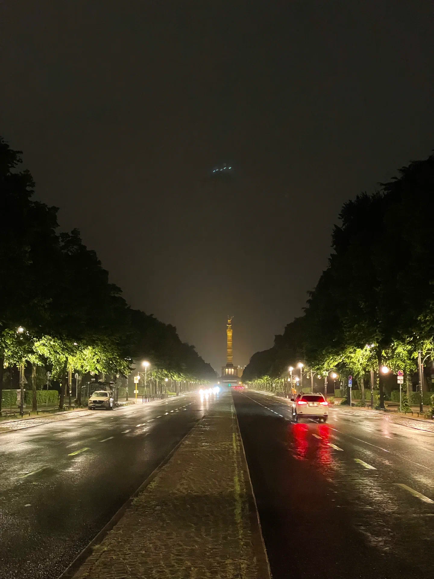 The Siegessäule at night, seen down a wet, tree-lined avenue