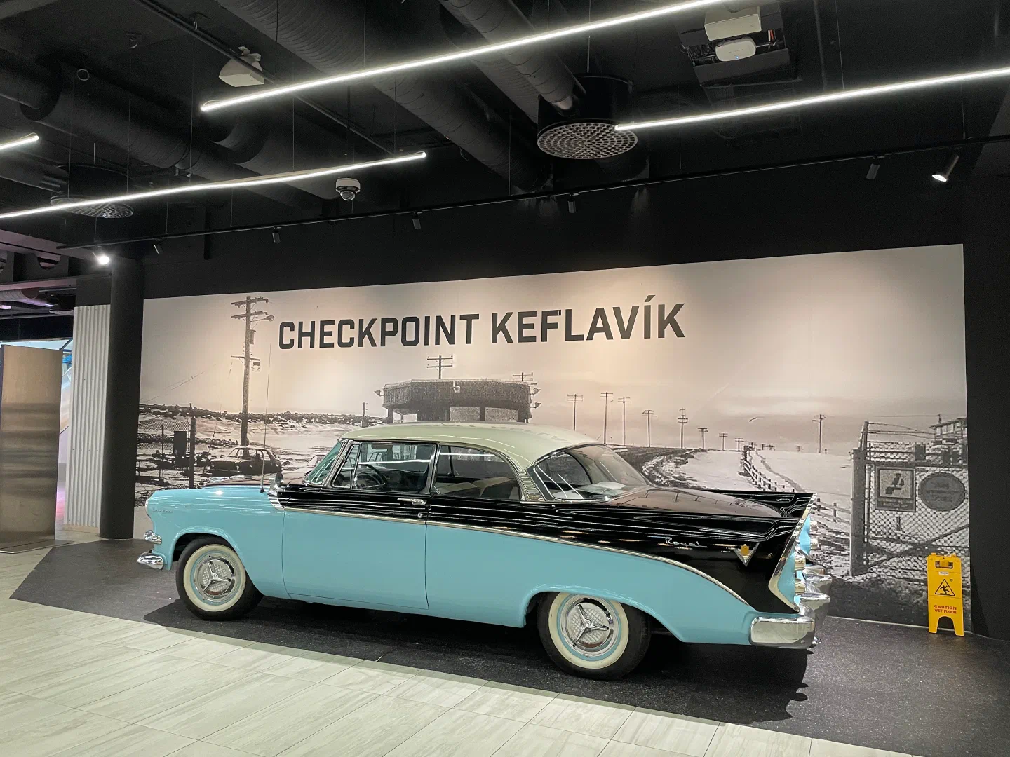 A restored two-tone 1950s Dodge Royal beneath a “Checkpoint Keflavík” mural