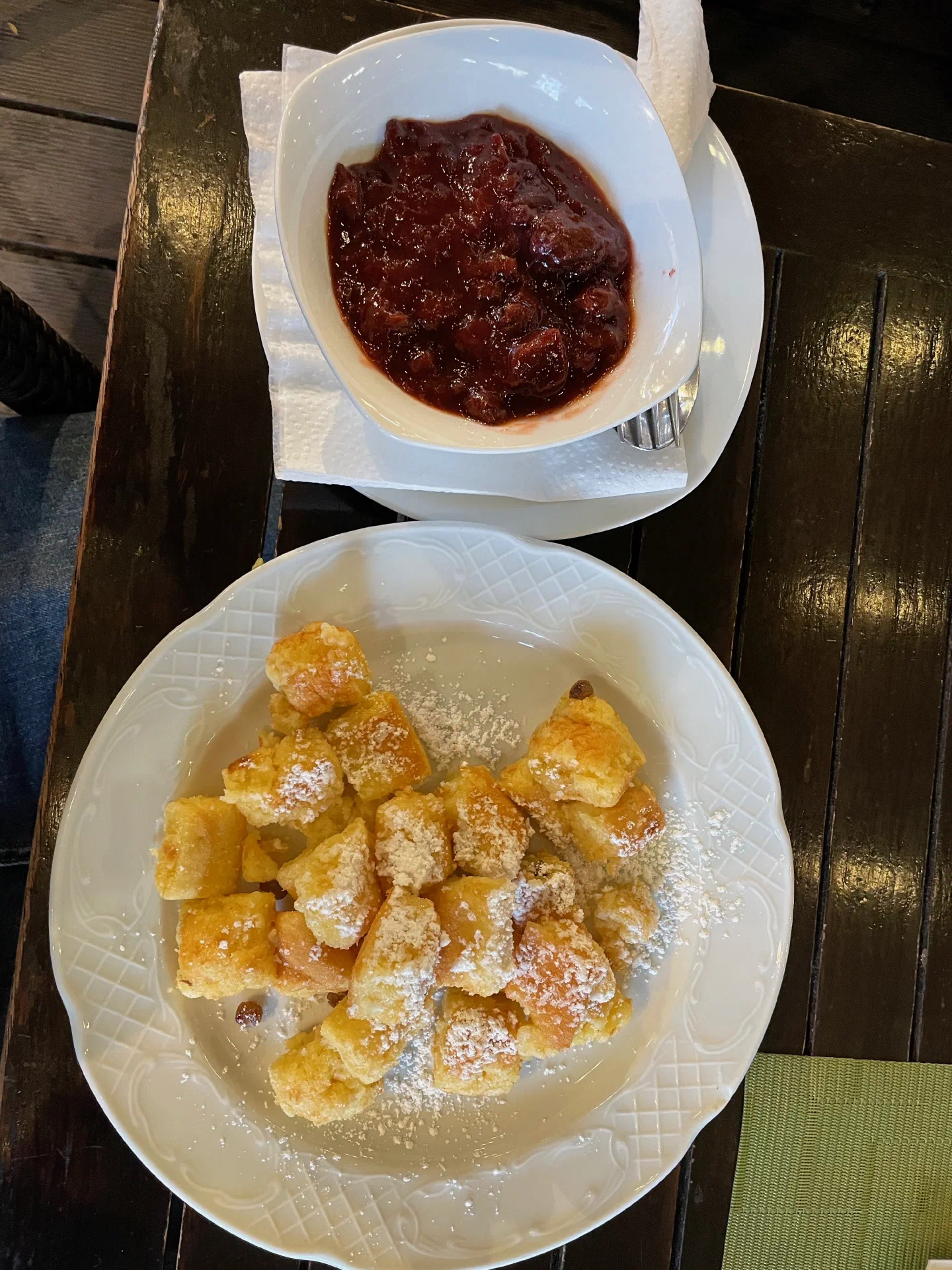 A plate of shredded Kaiserschmarrn dusted with icing sugar, with plum compote
