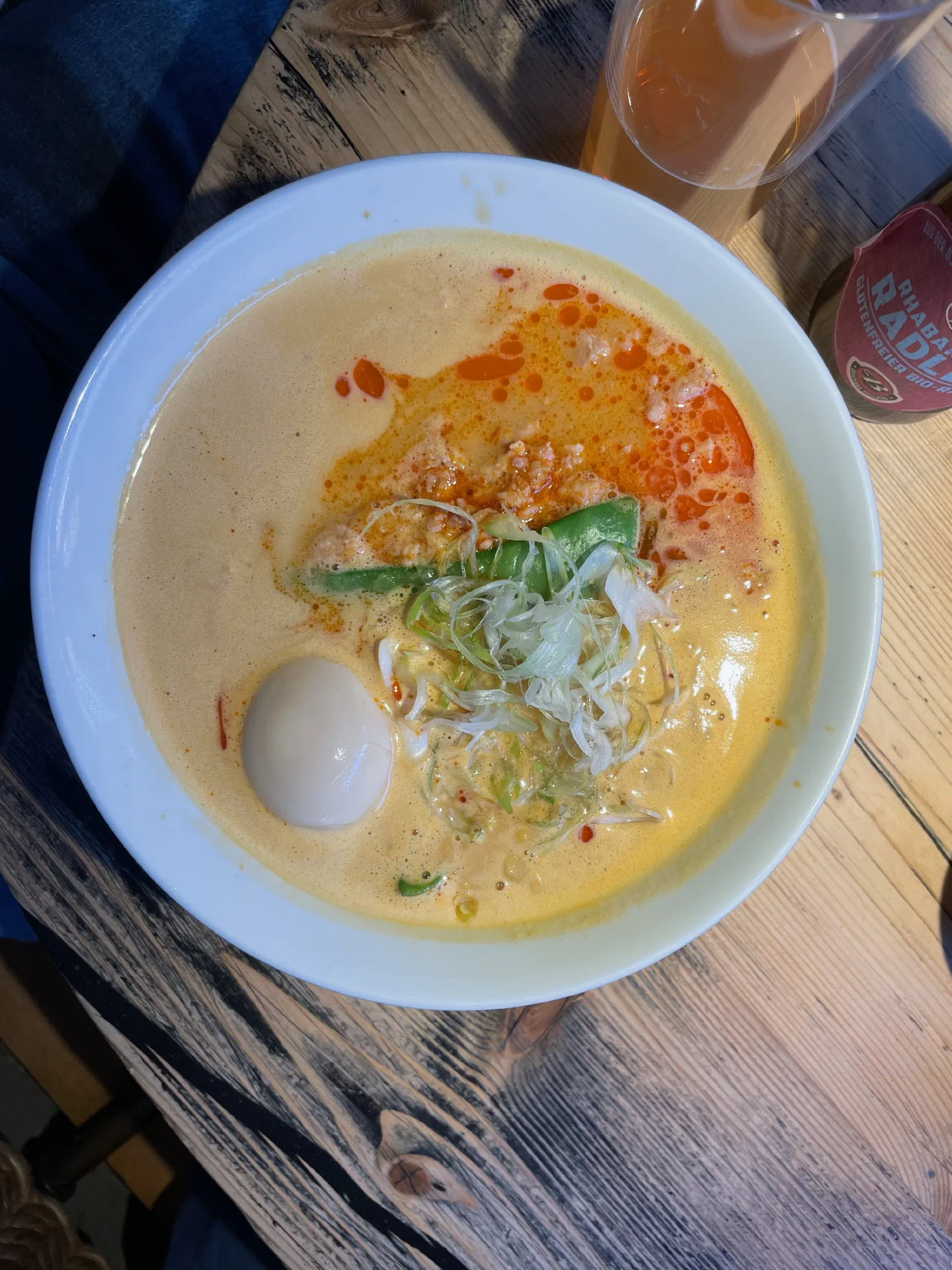 A bowl of creamy tantanmen ramen with a soft egg, beside a Radler